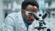 © visoot - A thoughtful African American male scientist, wearing a lab coat and safety goggles, working with a microscope in a high-tech laboratory, with various lab equipment in the background. Generative AI.