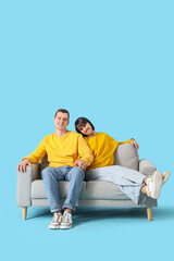 Wall Mural - Young couple in love holding hands on sofa against blue background