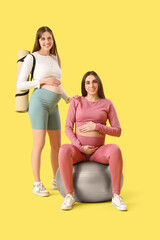 Poster - Pregnant female friends with fitball on yellow background