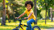 © Tanya - Happy smiling African American boy riding a bicycle in a park on a blurred natural background. Copy space.