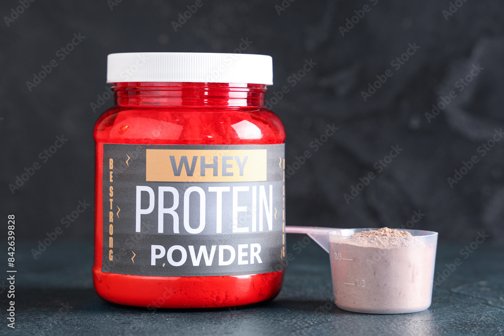Bottle and scoop with protein powder on dark background