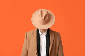 Wall Mural - Young man hiding face behind hat on orange background