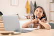© Pixel-Shot - Thoughtful little Asian girl with laptop studying online at home