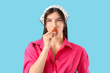 Poster - Beautiful young woman eating fresh strawberry on blue background