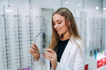 Wall Mural - A woman is smiling and holding a pair of glasses in a store. The store is filled with many different types of glasses