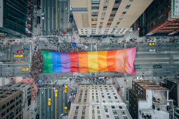 Wall Mural - High aerial view of a gay pride rainbow flag being carried by people through a city street