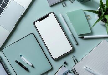 Wall Mural - A smartphone with a blank white screen on a work desk, surrounded by a laptop, notepad, and stationery