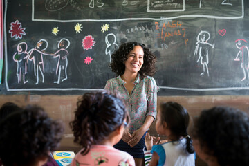 Empowering Education: A Young Teacher's Impact in a Disadvantaged Community smiling near the blackboard