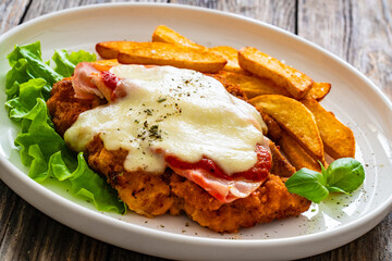 Wall Mural - Milanesa Napolitana - fried breaded cutlet with ham, mozzarella cheese and tomato sauce on wooden background
