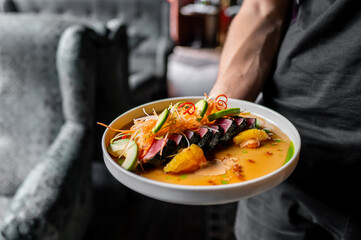 Close-up of a person holding a plate of colorful, gourmet food in a restaurant setting.