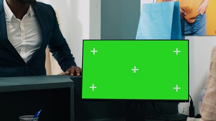Wall Mural - African american worker uses computer with greenscreen display on at checkout counter, putting clothes in a bag for customer. Employee looks at pc showing copyspace mockup screen. Camera A.