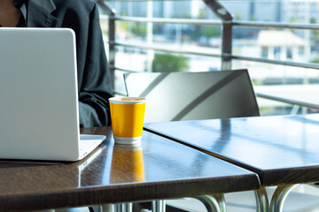 Person wearing a black suit, white laptop, and yellow coffee mug on a wooden table