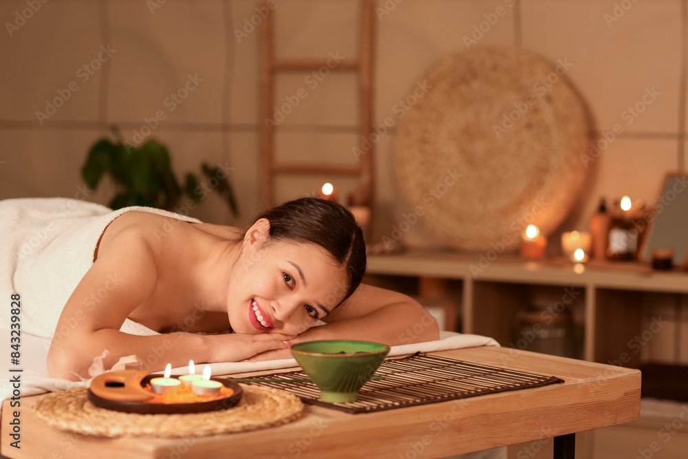 Beautiful Asian woman lying on table in dark spa salon