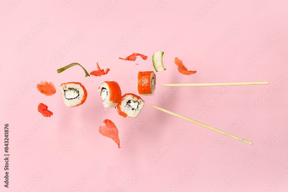 Tasty flying sushi rolls, ginger, cucumber and chopsticks on pink background