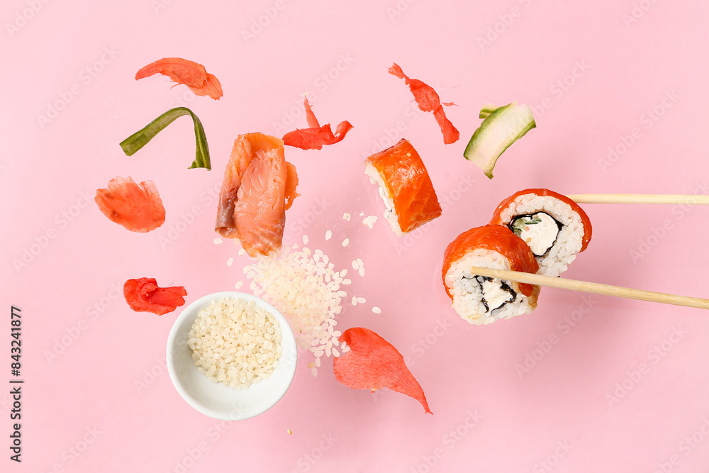 Tasty flying sushi rolls, ingredients and chopsticks on pink background