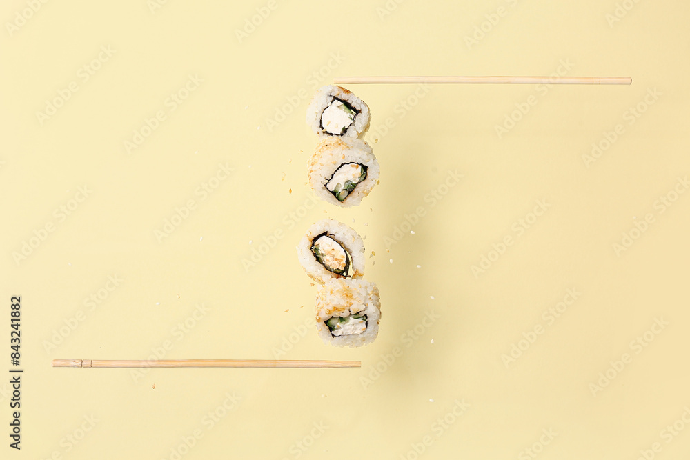 Tasty flying sushi rolls and chopsticks on beige background