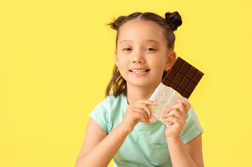 Canvas Print - Cute little Asian girl with chocolate bar on yellow background, closeup