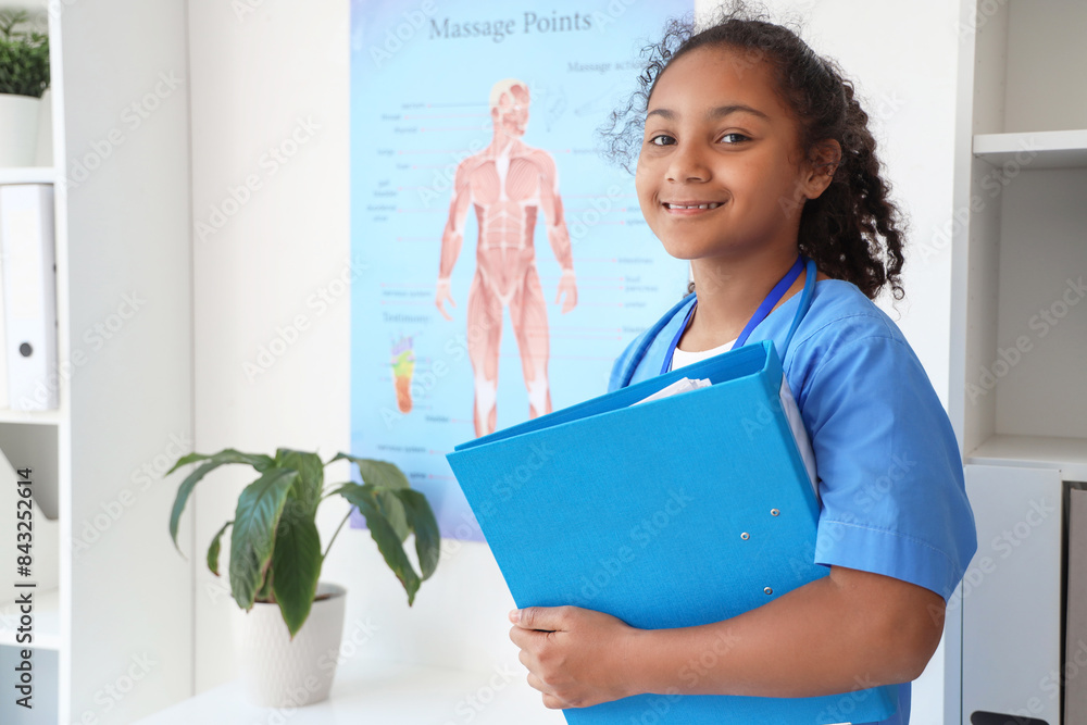 Little African-American doctor with folder in clinic