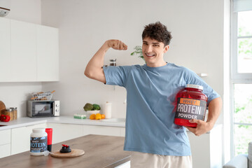 Canvas Print - Sporty young man with protein powder showing muscles in kitchen