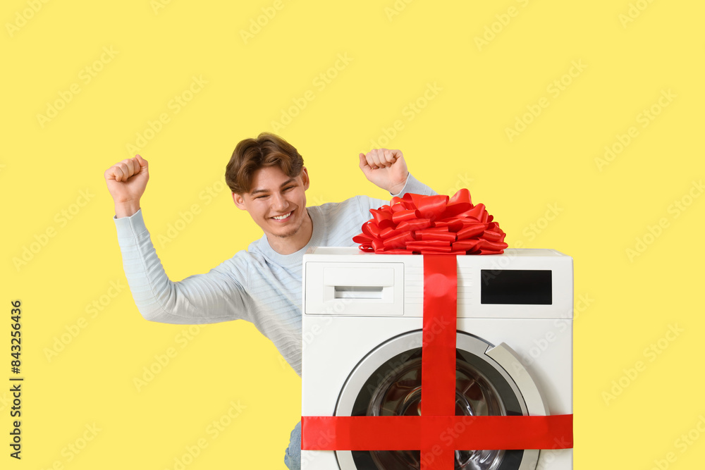 Happy young man with gift washing machine on yellow background