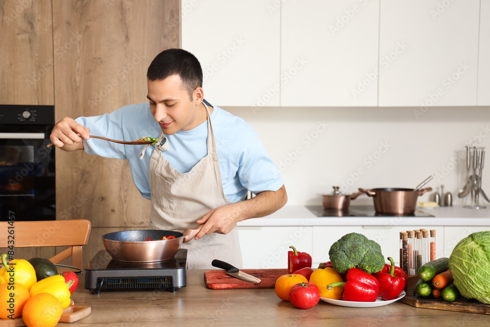 Young man frying vegetables in kitchen