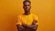 © evgenia_lo - A confident young African American man in a yellow shirt stands with his arms crossed against an orange background.