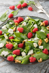 Wall Mural - Summer salad of spinach, raspberries, feta and walnuts close-up in a plate on the table. Vertical