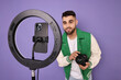 © New Africa - Technology blogger reviewing camera and recording video with smartphone and ring lamp on purple background