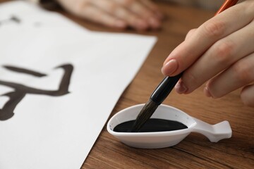 Wall Mural - Calligraphy. Woman dipping brush into inkwell at wooden table, closeup