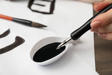 Wall Mural - Calligraphy. Woman dipping brush into inkwell at table, closeup