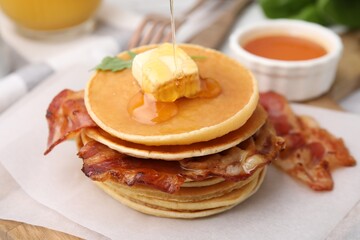 Wall Mural - Pouring honey onto delicious pancakes with bacon at table, closeup