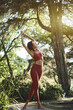 © insta_photos - Authentic candid vertical photo or fit sporty young Hispanic woman wearing sportswear meditating doing yoga breathing stretching exercises standing in nature park or forest outdoors in sunny morning.