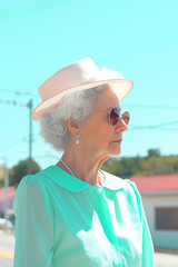 Wall Mural - A woman wearing a green dress and a white hat is standing on a street