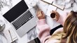 © yj - an influencer typing on her laptop with notes beside her, as she sits at a table in front of her white marble desk. on the desk are a phone, laptop, notebook and coffee cup. generative AI