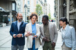 © Marko Geber - Group of diverse business professionals walking and looking at a smartphone on a city street