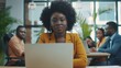 © The Little Hut - Attractive african young confident businesswoman sitting at the office table with group of colleagues in the background working on laptop computer : Generative AI