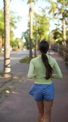 Wall Mural - A woman is enjoying a morning jog in a park surrounded by lush trees and rustic wooden fences