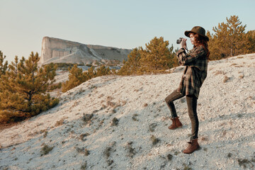 Wall Mural - Woman in hat and plaid shirt standing on hilltop with mountain in background