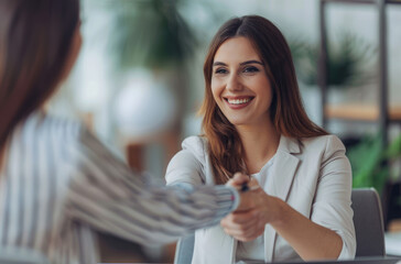 Wall Mural - A young businesswoman shaking hands with an employee at her desk in the office, smiling and holding papers during a job interview