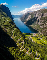 Wall Mural - winding road snaking its way up a steep mountainside overlooking a serene fjord in Norway. The road is flanked by lush green vegetation and towering cliffs. Kjerag, Lysebotn, Lysefjorden, Norway