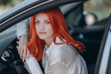 red-haired woman sits confidently in the driver's seat of a grey sedan, her face framed by cascading