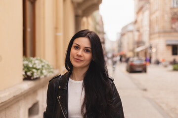 Outdoor portrait of beautiful brunette woman standing on the street, walking outdoors. Girl wear black leather jacket. Tourist woman walking outside.