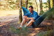 © baranq - Man sitting in hammock using mobile phone in forest