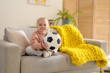 Wall Mural - Cute little girl with soccer ball sitting on sofa at home