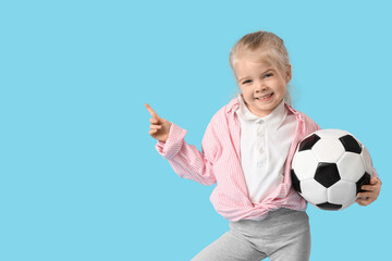 Wall Mural - Cute little girl with soccer ball pointing at something on blue background