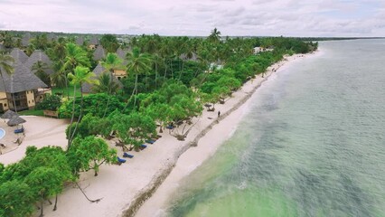 Wall Mural - Aerial view of green palms, bungalows, white sandy beach, ocean with waves at sunset in summer. Top drone view of wooden houses, sea with azure water, palms. Luxury resort in Zanzibar. Tropical