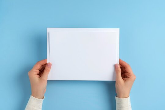 Female hands holding blank white paper sheet on light blue background. Top view. Mockup paper with copy space for text, Generative AI