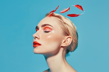 Wall Mural - A woman with vibrant makeup and striking red lipstick poses against a blue background, adorned with red feathers in her hair, showcasing a creative and artistic fashion style