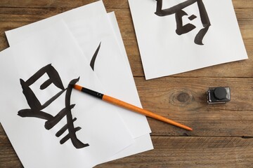 Wall Mural - Calligraphy. Papers with written hieroglyphs, inkwell and brush on wooden table, flat lay