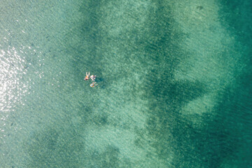 Wall Mural - People swim in Greece transparent turquoise blue sea water with sandy bottom, aerial drone view.